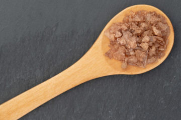 Single wooden teaspoon with rock salt shot on grey slate from above with copyspace for text