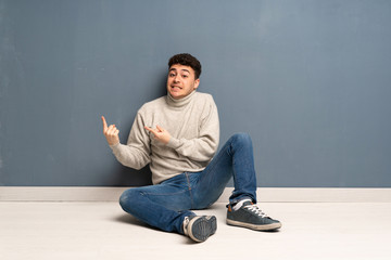 Young man sitting on the floor frightened and pointing to the side