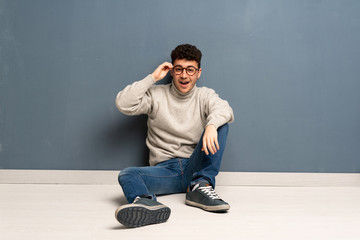 Young man sitting on the floor with glasses and surprised