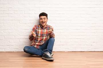 Young man sitting on the floor pointing to the front and smiling