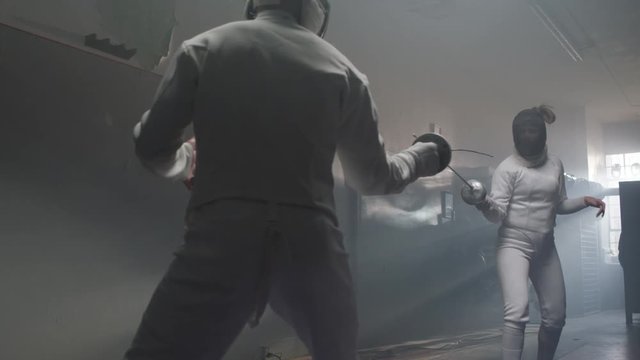Push-in on a female fencer deflecting an attack and going in for an attack in a dark and moody fencing gym