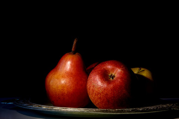 The pear and the apple are illuminated by sunlight against a dark background. The image is similar to the picture. Concept - fruit diet
