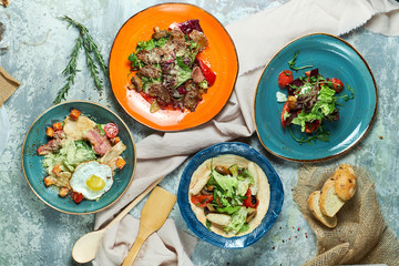 Multi-colored plates with different salads. Beautiful serving of dishes. Light gray background. Restaurant menu