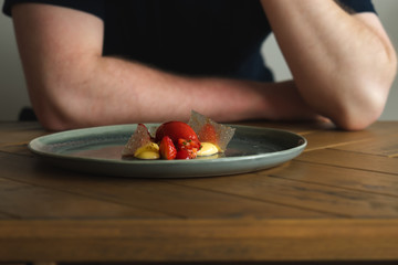 Young aspiring Chef looks contently, with his arms folded, at the modern dessert made of Strawberry, White chocolate,Tarragon and Sichuan Pepper. Dish Designed and created by the Chef, unique dish.