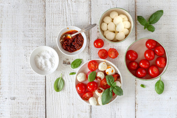 Small bowls with colorful ingredients of Caprese salad on a white wooden table, flat lay style