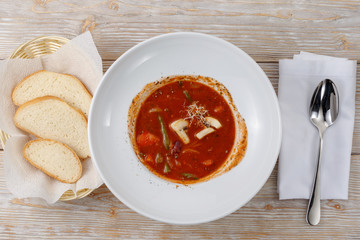 Plate of tomato soup with vegetables, bread and spoon on wooden background