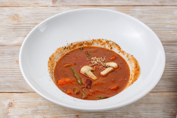 Plate of tomato soup with vegetables and micro green on wooden background