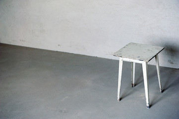 Old white stool against the backdrop of a gray plaster wall. White chair on the floor.