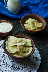 Dumplings with potatoes and cabbage. Sour cream, milk and greens. Traditional dish of Ukraine. Dark wooden background.