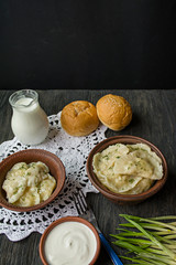 Dumplings with potatoes and cabbage. Sour cream, milk and greens. Traditional dish of Ukraine. Dark wooden background.