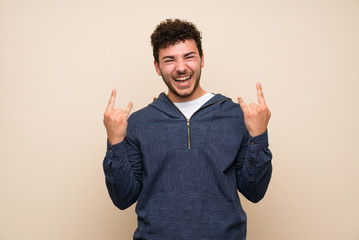 Man with curly hair over isolated wall making rock gesture