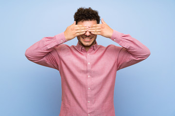 Man with curly hair over isolated blue wall covering eyes by hands