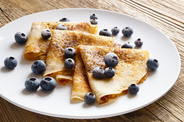 a portion of pancakes with wimberry, and sugar powder on  wooden top