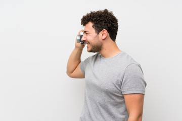 Man with curly hair over isolated wall holding a camera