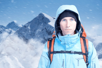Fototapeta na wymiar Young male mountain climber on winter mountain top view looking at camera. Front view. Active lifestyle and tourism in cold weather. Winter mountain landscape and cloudy sky.