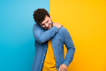 Man with curly hair over colorful wall suffering from pain in shoulder for having made an effort
