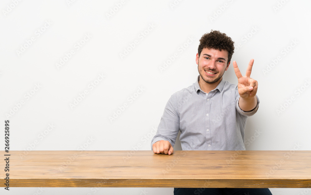 Wall mural young man with a table smiling and showing victory sign