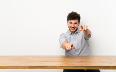 Young man with a table points finger at you while smiling