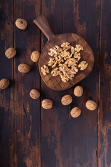 Cracked and whole walnuts lying on cutting board and wooden table, top view. Healthy nuts and seeds composition.