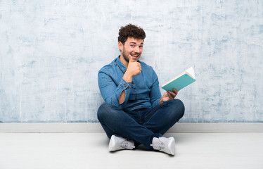 Young man sitting on the floor holding and reading a book