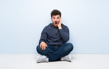 Young man sitting on the floor with surprise and shocked facial expression