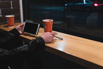 Girl holding smartphone in hand, sit in cafe, working, pen, use gadget. Network, wifi, social, communication. Freelancer works remotely. Online marketing. Night city, dark theme. copy space