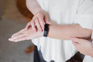 An elderly woman in a white blouse is wearing a fitness bracelet. Smart watch on the hand of an old...