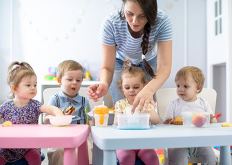 Group of nursery babies toddlers eating healthy food lunch break together with kindergartener