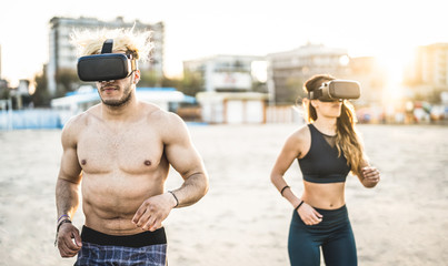 Young couple running at beach with virtual reality goggles headset - Sport and technology concept with friends jogging and exercising on trek simulation on summer time - Contrast sunset filter
