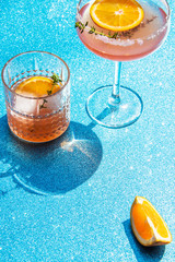 Grapefruit and thyme cocktails, refreshing drinks with ice on a light blue background. Summer garden party still life with orange and cold drinks, trendy retro style with artistic shadows.