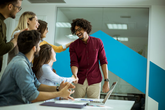 Group of young coworkers interacting around a table and handshaking in the office