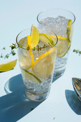Lemonade or mojito cocktail with lemon and lime, cold refreshing drink or beverage with ice on a light blue backround. Retro style with artistic trendy shadows.