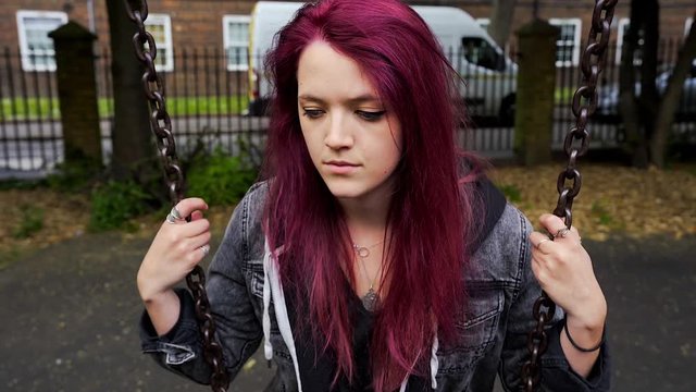 emo girl with purple hair pondering about life by the swing in the playground close up