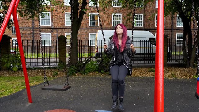 emo girl with purple hair pondering about life by the swing in the playground