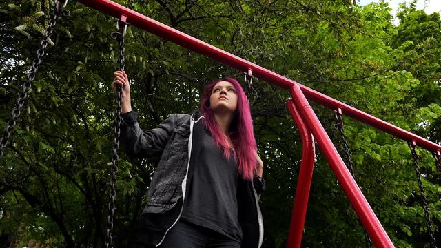 emo girl standing on the swing and feeling annoyed and bored