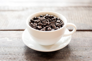 Coffee beans in a mug on a wooden table.