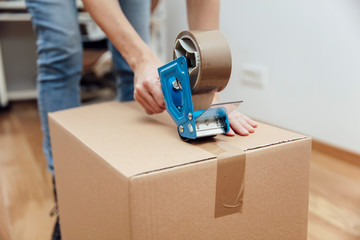 Hands of a man using a tape dispenser to seal a shipping box