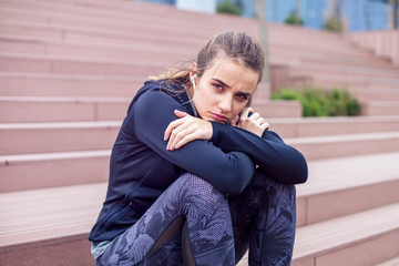 Worried young woman sits outside on the stairs