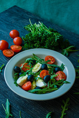 Greek salad with fresh tomatoes, arugula, eggs, olives with olive oil on a dark wood background. Healthy food. Veggie dish.