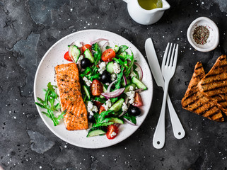 Healthy balanced lunch - grilled red fish fillet salmon and vegetables, olives, feta salad on dark background, top view
