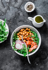 Spicy chickpeas, baked salmon, crispy radish, arugula salad on a dark background, top view