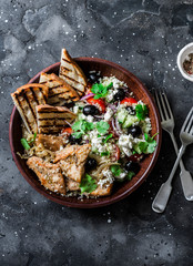 Mediterranean style lunch - couscous, cherry tomatoes, cucumbers, feta cheese, olives salad and lemon herbs roasted chicken breast on dark background, top view
