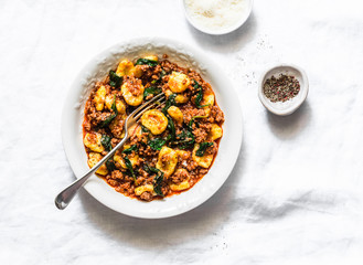 Potato turmeric gnocchi with bolognese sauce and spinach on a light background, top view