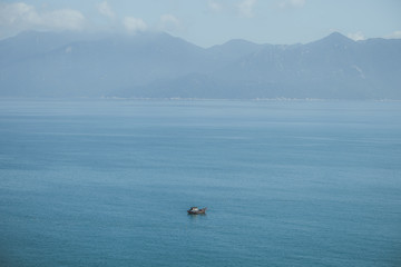 View of one boat in a blue endless bay in Vietnam with mountains in the background on a sunny day