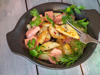 Hot breakfast with fried potatoes and turkey steak on a black plate with herbs, bread buns and coarse salt in a salt shaker made of clay