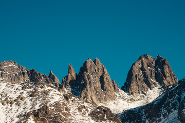 Pointed cliffs against a bright blue sky. Snow lies at the base. Free space for text