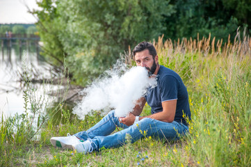 Stylish brutal smoker smoking an electronic cigarette in the daylight. Non-tobacco smoking.