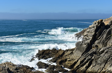 Fototapeta na wymiar Cliff with waves breaking, mist and blue sky. Galicia, Spain.
