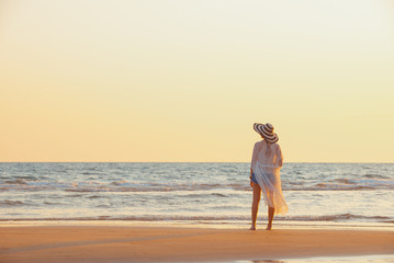A young woman stands on the beach during a sunset, summer vacation.