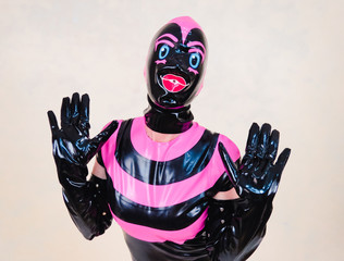 Hooded woman holding up gloved hands in expression of shock or surprise. Pink and black rubber...